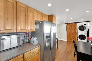 Kitchen with stainless steel refrigerator with ice dispenser, light wood-type flooring, stacked washing maching and dryer, crown molding, and decorative backsplash