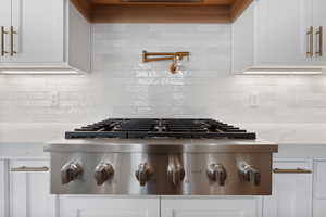 Room details with stainless steel gas stovetop, white cabinets, and backsplash