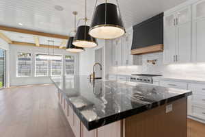 Kitchen with glass insert cabinets, tasteful backsplash, a large island with sink, premium range hood, and light wood-style floors