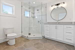 Full bathroom featuring a shower stall, vanity, tile patterned floors, baseboards, and toilet