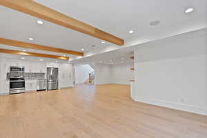 Unfurnished living room featuring recessed lighting, baseboards, light wood-type flooring, beamed ceiling, and stairway