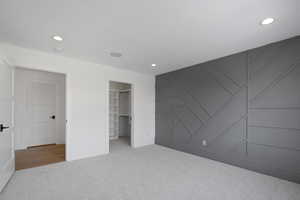 Unfurnished bedroom featuring a decorative wall, baseboards, recessed lighting, a spacious closet, and carpet