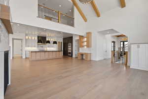 Unfurnished living room featuring beam ceiling, light wood-style floors, baseboards, high vaulted ceiling, and a chandelier