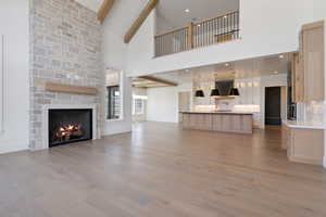 Unfurnished living room with light wood finished floors, a stone fireplace, baseboards, a towering ceiling, and beamed ceiling
