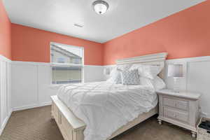 Bedroom featuring dark carpet, visible vents, a wainscoted wall, and a decorative wall