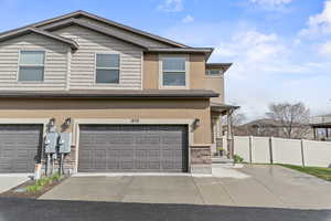 View of front of house featuring stucco siding, fence, stone siding, an attached garage, and driveway