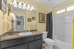 Bathroom with toilet, shower / bathtub combination with curtain, vanity, and visible vents