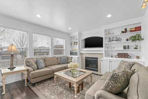 Living room with dark wood-type flooring, recessed lighting, a glass covered fireplace, and a textured ceiling