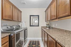 Laundry room featuring visible vents, separate washer and dryer, a sink, a textured ceiling, and cabinet space