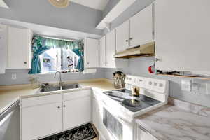 Kitchen featuring white range with electric stovetop, dishwasher, a sink, under cabinet range hood, and white cabinetry