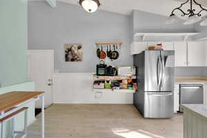 Kitchen featuring white cabinets, light countertops, appliances with stainless steel finishes, light wood-type flooring, and a wainscoted wall