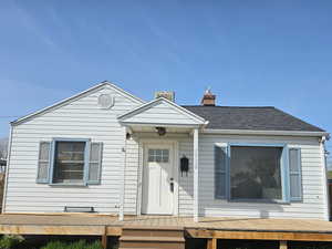 View of front of home featuring roof with shingles, a deck, and a chimney