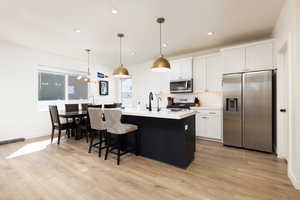 Kitchen featuring light countertops, white cabinets, light wood-style floors, decorative backsplash, and appliances with stainless steel finishes