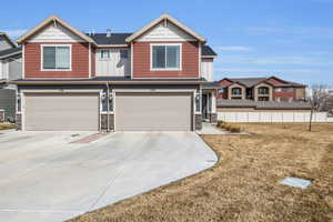 View of front of property with board and batten siding, a garage, stone siding, and driveway