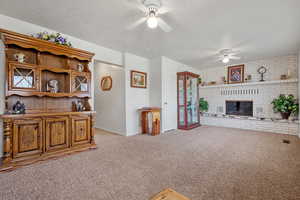 Living room with visible vents, a ceiling fan, a fireplace, a textured ceiling, and light colored carpet