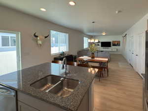 Kitchen featuring dark stone countertops, dishwasher, a sink, open floor plan, and light wood finished floors