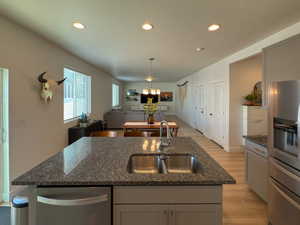 Kitchen with light wood-type flooring, dark stone countertops, open floor plan, a kitchen island with sink, and a sink