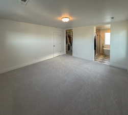 Unfurnished bedroom featuring a walk in closet, visible vents, baseboards, and light colored carpet