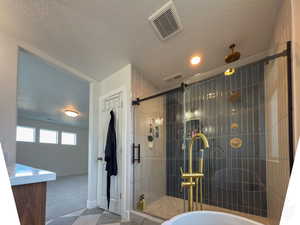 Bathroom featuring baseboards, a bathtub, a textured ceiling, a shower stall, and visible vents