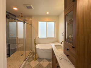 Full bath featuring vanity, a stall shower, a soaking tub, a textured ceiling, and visible vents