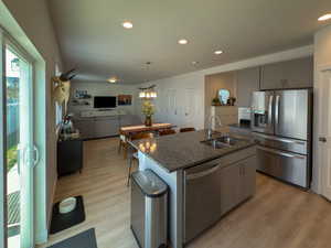 Kitchen featuring a sink, appliances with stainless steel finishes, light wood-style floors, recessed lighting, and dark stone counters