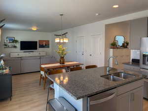 Kitchen with light wood-style floors, dark stone countertops, dishwasher, a sink, and a center island with sink