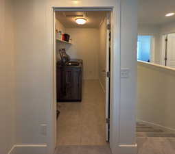 Hall with independent washer and dryer, light tile patterned floors, and baseboards