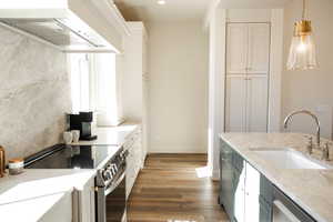 Kitchen featuring appliances with stainless steel finishes, wood finished floors, a sink, decorative light fixtures, and custom range hood