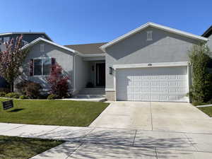 Ranch-style house with an attached garage, a front lawn, driveway, and stucco siding