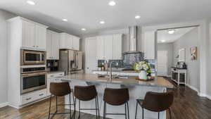 Kitchen featuring a kitchen breakfast bar, wall chimney range hood, backsplash, appliances with stainless steel finishes, and a sink