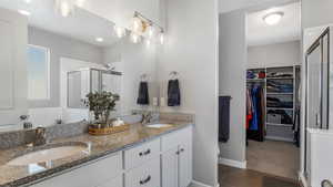 Full bathroom with a shower stall, double vanity, a sink, and a spacious closet