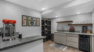 Bar with indoor wet bar, recessed lighting, light wood-style flooring, beverage cooler, and a sink