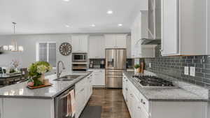 Kitchen featuring backsplash, dark wood-type flooring, wall chimney exhaust hood, stainless steel appliances, and a sink