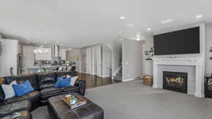 Living area featuring dark colored carpet, a chandelier, stairway, visible vents, and a tile fireplace