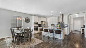 Kitchen featuring wall chimney exhaust hood, tasteful backsplash, a breakfast bar, appliances with stainless steel finishes, and a center island with sink