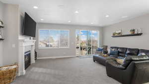 Living area featuring light carpet, a glass covered fireplace, baseboards, and recessed lighting
