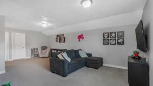 Carpeted living area with baseboards, attic access, and lofted ceiling