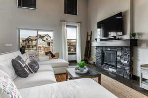 Living area with wood finished floors, a towering ceiling, a stone fireplace, and a wealth of natural light