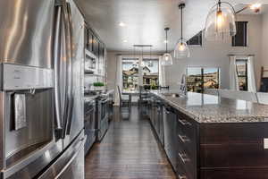 Kitchen with a sink, an island with sink, a textured ceiling, dark wood-style floors, and stainless steel appliances