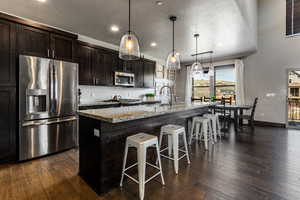 Kitchen with a sink, appliances with stainless steel finishes, a kitchen bar, dark wood-style floors, and a center island with sink
