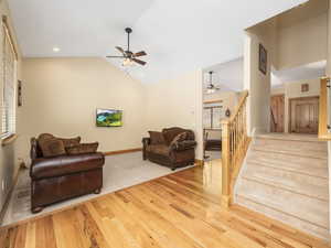 Living area featuring ceiling fan, wood finished floors, stairs, baseboards, and high vaulted ceiling