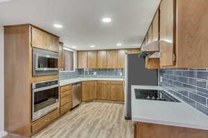 Kitchen featuring light wood-type flooring, under cabinet range hood, brown cabinets, appliances with stainless steel finishes, and a sink
