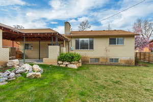 Rear view of property with a patio, a chimney, brick siding, a yard, and fence