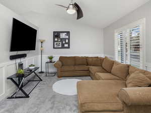 Carpeted living room with wainscoting, a decorative wall, a ceiling fan, and lofted ceiling