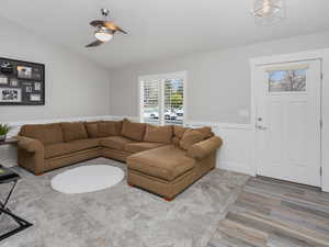 Living room featuring a lofted ceiling, wainscoting, ceiling fan, a decorative wall, and LVP floors