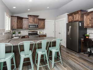 Kitchen with a sink, LVP flooring, appliances with stainless steel finishes, backsplash, and lofted ceiling