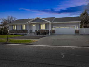 View of front of house featuring an attached garage, driveway, fence, and stone siding