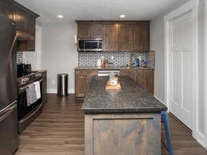 Basement Kitchen with a sink, appliances with stainless steel finishes, under cabinet range hood, LVP flooring, and backsplash