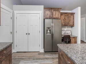 Kitchen with light stone countertops, LVP floors, pantry, decorative backsplash, and stainless steel fridge