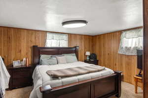 Bedroom with wooden walls, light colored carpet, and a textured ceiling